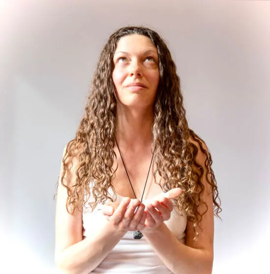 Leah Fae holding a crystal, gazing upward in soft light